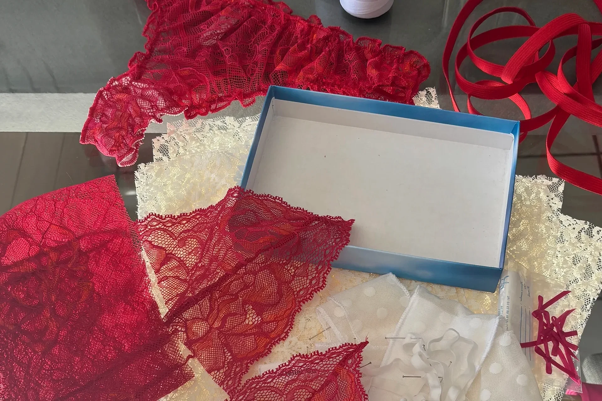 Dentelle rouge découpée et fils de couture étalés sur la table de l’atelier
