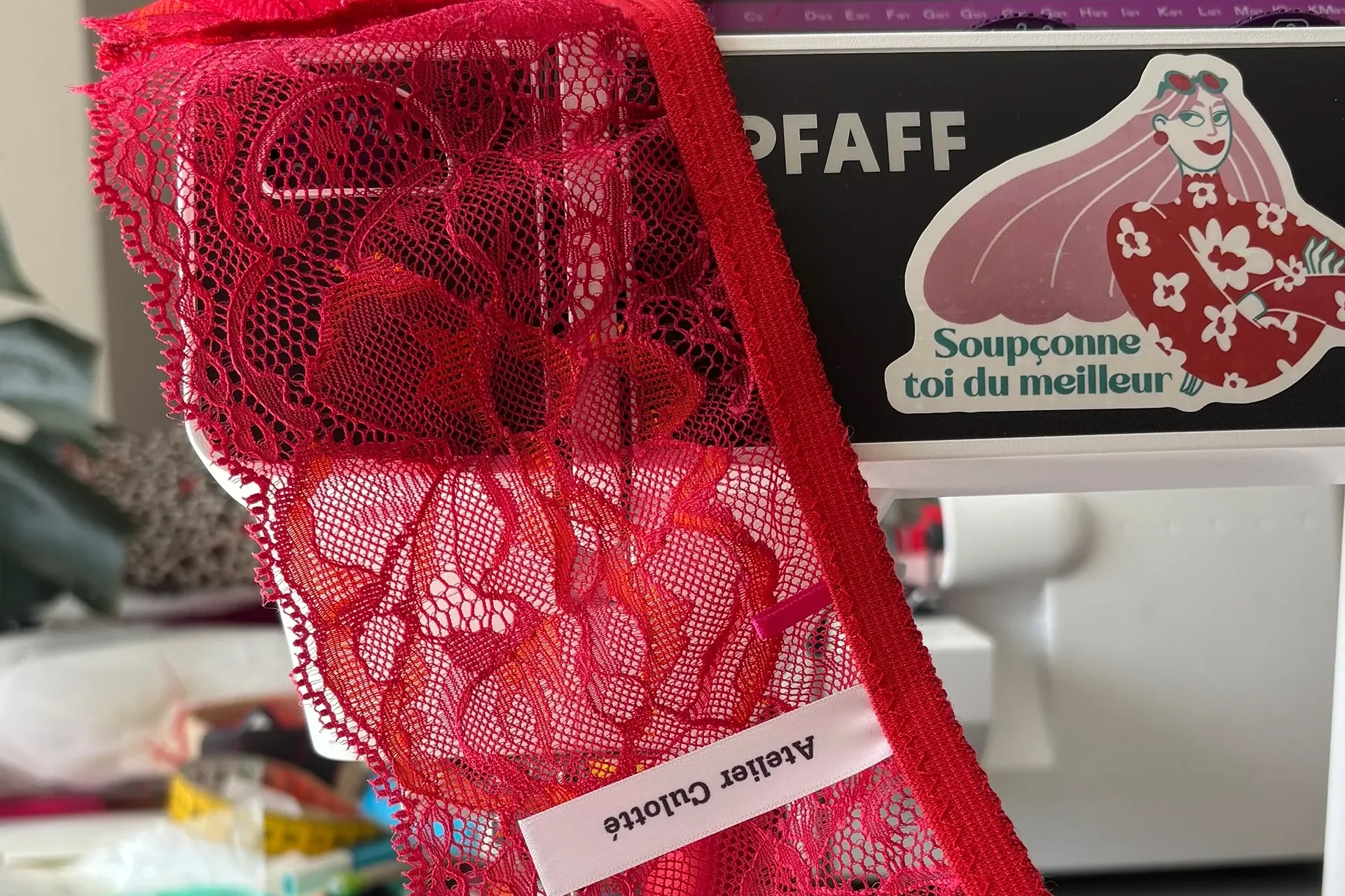 Une pièce de dentelle rouge en cours de couture, posée sur la table de l’atelier près d’une machine à coudre