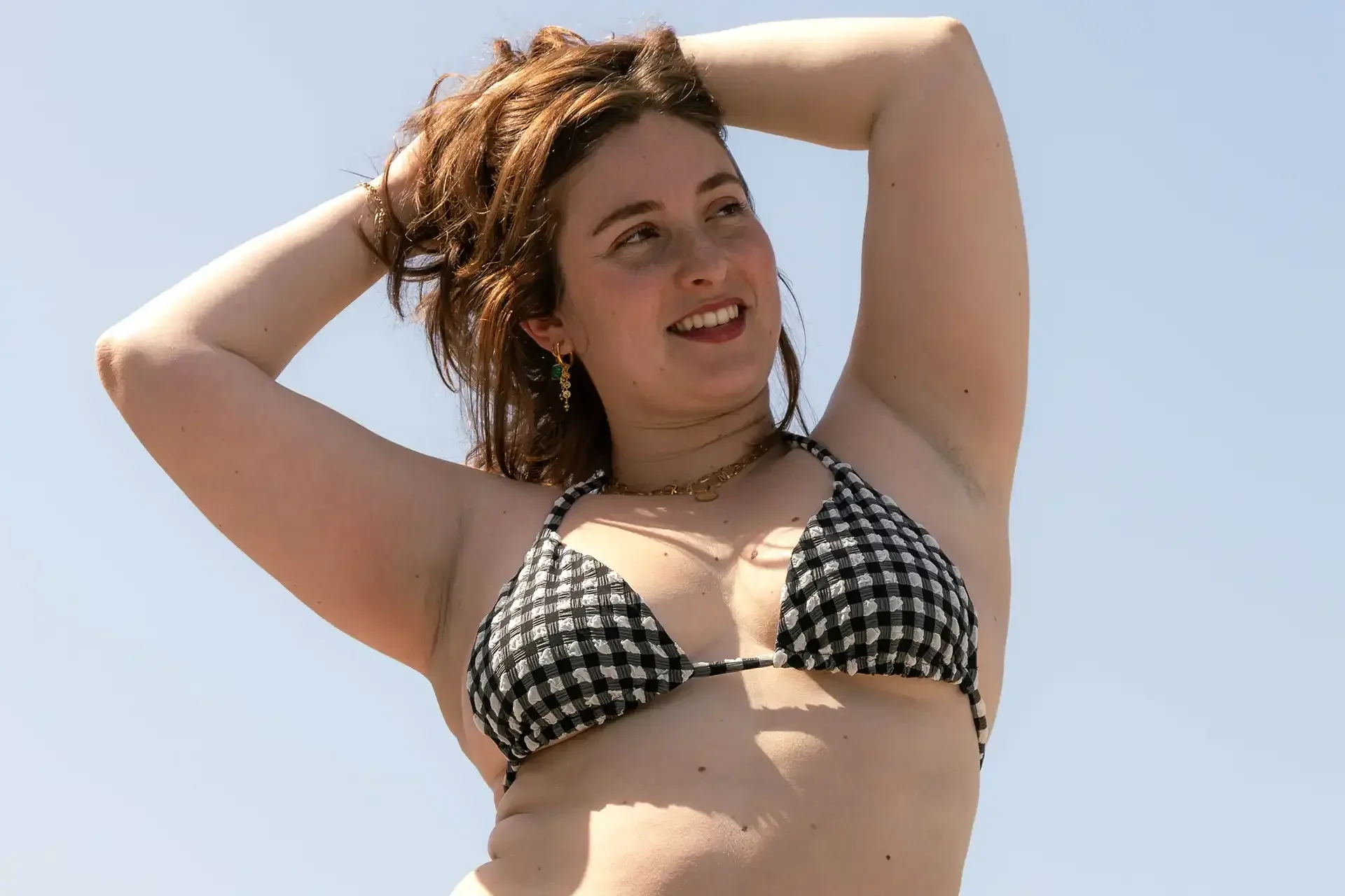 Une femme en bikini vichy, les bras levés, sous un ciel bleu
