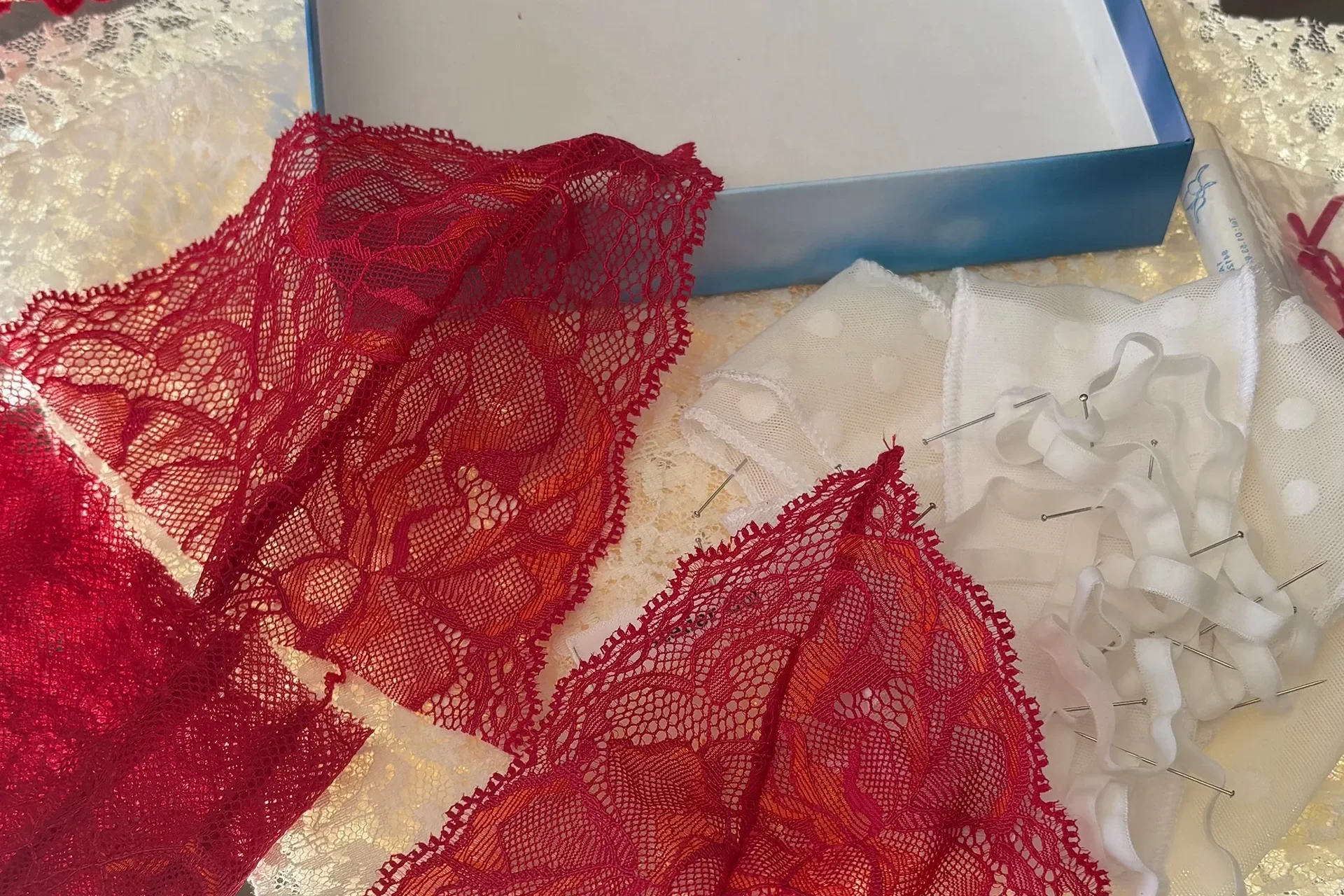 Dentelle rouge et pièces découpées étalées sur la table de l’atelier, près d’une boîte